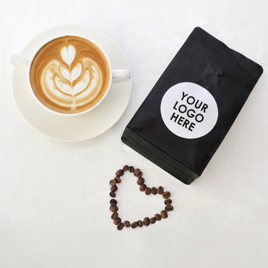 Black coffee bag with a logo next to a bowl of coffee beans on a white surface